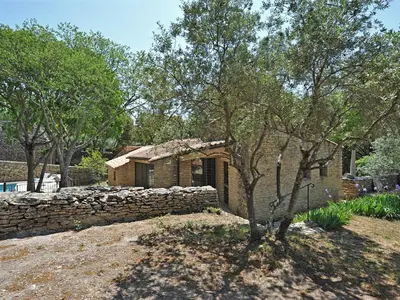 a stone house with a stone wall and a tree at Le Chant des Bories in Gordes
