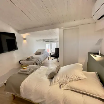 two beds in a room with white walls and a tv at Centre Historique Appartement Climatisé avec terrasse in Aix-en-Provence