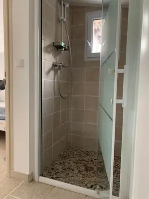 a shower with a glass door with a pebble floor at Studio le soleil couchant in Saint-Saturnin-lès-Avignon