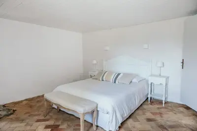 a white bedroom with a white bed and a stool at Le Bas Château Provence Luberon in Saint-Michel-lʼObservatoire