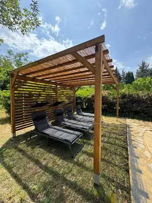 a wooden pergola with lounge chairs under it at La maison vauclusienne in Carpentras