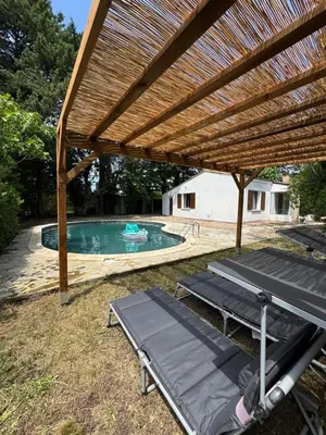 a wooden pergola over a swimming pool with two chaises at La maison vauclusienne in Carpentras