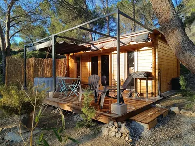 a small wooden cabin with a porch and two chairs at Escapade sous les pins 20m2 in Aurons