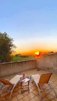 two chairs and a table on a patio with the sunset at Maison provençale au milieu des champs in Robion en Luberon