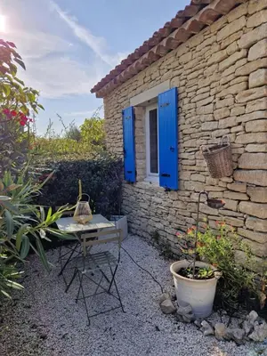 a patio with a table and a window with blue shutters at Le Bastidon des Mésanges in Gordes
