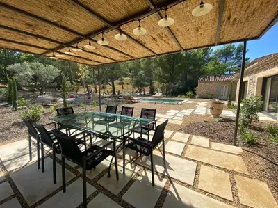 a patio with a glass table and chairs under a pergola at Bastide Farandole in Eygalières
