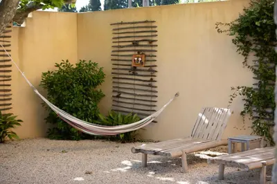 a hammock and a bench next to a wall at sous la glycine de costebelle in Cheval-Blanc