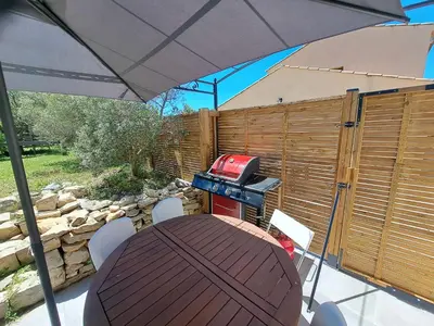a patio with a table with an umbrella and a grill at Gîte Le Dodo in Lançon-Provence