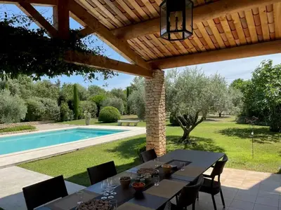 a dining table under a pergola next to a swimming pool at La bastide le Jucamas in Saint-Saturnin-les-Apt