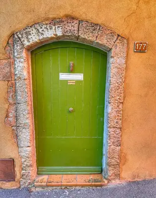a green door in a building with a stone wall at Les 3 Terrasses in Roussillon