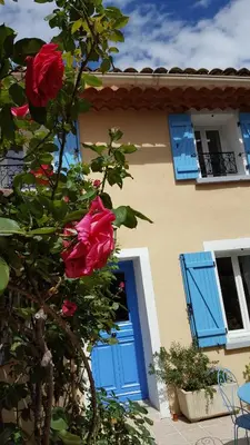 a house with a blue door and a tree with roses at La Calvinette in Pernes-les-Fontaines