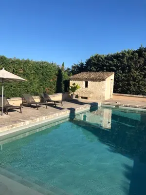 a swimming pool with two chairs and an umbrella at Gîte Les Alpilles in Eygalières