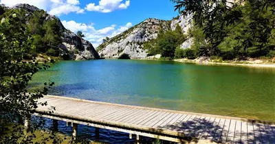 a wooden walkway over a lake with a mountain at Mazet Arlequine in Eygalières