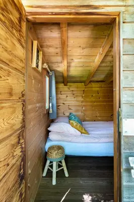 a small bed in a wooden cabin with a stool at Cabane Perchée avec Jacuzzi, au Coeur du Luberon in Oppède