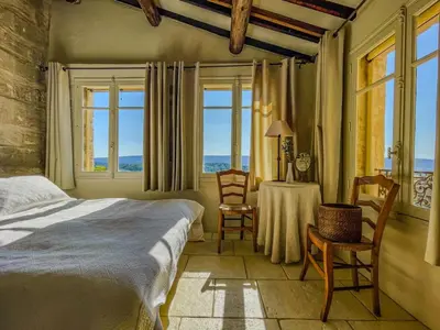 a bedroom with a bed and a table and windows at Maison de charme au coeur du village de Gordes in Gordes