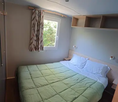 a small bedroom with a bed with a window at Mobilhome 6 personnes in Cheval-Blanc