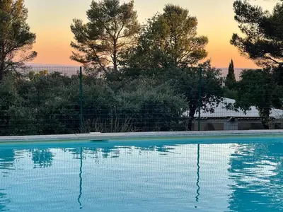 a blue swimming pool with a sunset in the background at Gîte Le Provence Spacieux 100m2 in Saumane-de-Vaucluse