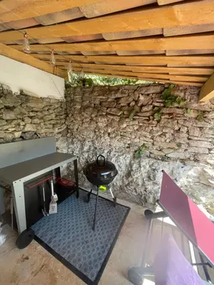 a barbecue under a stone wall with a table and a grill at La l isloise in LʼIsle-sur-la-Sorgue