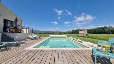 a swimming pool on a wooden deck with chairs on a patio at Lou Miradou in Maubec