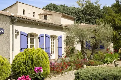 a house with blue windows and flowers in a garden at MAISON de CHARME in Cavaillon