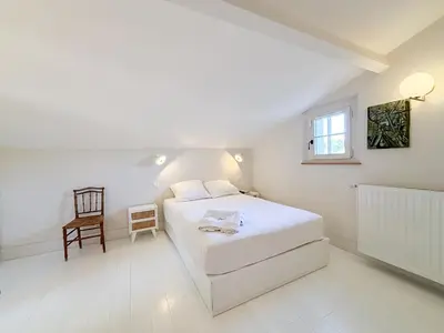 a white bedroom with a bed and a chair at Mas des Collines in Saint-Hippolyte-le-Graveyron