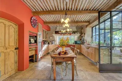 a kitchen with orange walls and a wooden table at MAS DES CIGALES Lambesc in Lambesc