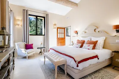 a white bedroom with a large bed and a chair at La Villa des Cedres in Bonnieux