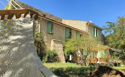 a stone house with green windows and a yard at Authentique mas provençal avec piscine in Beaumont-de-Pertuis