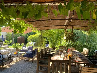 a wooden table under a pergola in a garden at Chambres et table d'hôtes Au Brabo in Mormoiron