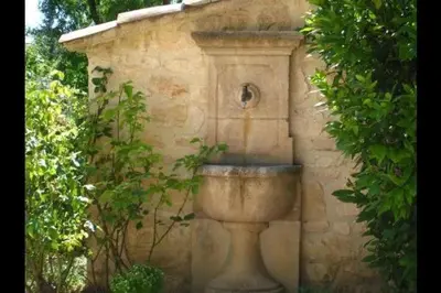 a stone fountain in front of a stone wall at Gîte une treille en provence in Saint-Didier
