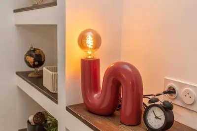 a red candle with a light on a shelf with a clock at Suite Vert Provence - Hypercentre - Wifi in Apt