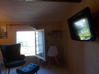 a living room with a tv and a chair and a window at Tramontane chambre salon et piscine in Jonquerettes