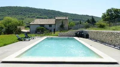 a swimming pool in front of a stone house at Chambre d'hôte dans ferme provençale in Banon