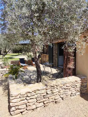 a stone wall with a tree in front of a house at Le Mas Natán in Gordes