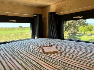 a book sitting on a bed in a room with windows at La Tiny House des Vignes du Château de Vauclaire in Meyrargues