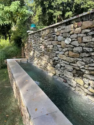 a stone retaining wall with a pool of water at Les goûts et les couleurs in Cucuron