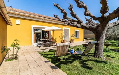 a yellow house with two chairs and a tree at 2 Bedroom Amazing Home In Noves in Noves