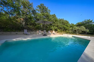 a swimming pool with an umbrella and chairs and a table at Le MAS DES VERGIERS in Murs