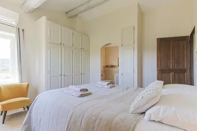 a white bedroom with a bed and a chair at Villa Vue Luberon in Gordes