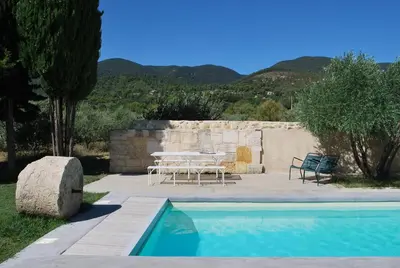 a pool with a table and chairs next to a wall at La Grande Bastide in Vaugines