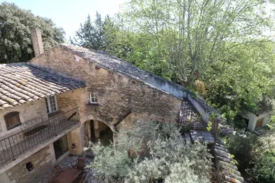 an old stone house with a balcony and trees at Les 2 voûtes - Mas provençal pour 10 personnes in Oppède