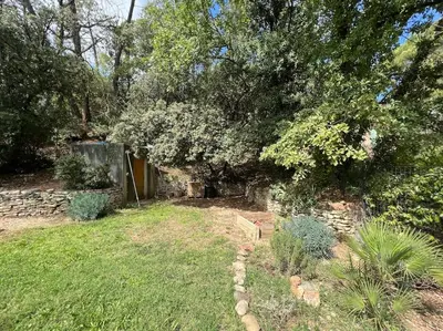 a backyard with a stone wall and trees and grass at Villa climatisée avec piscine in Gordes