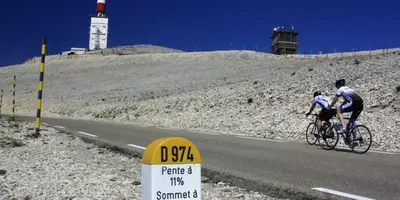 two people riding bikes on a road with a lighthouse in the background at Le temps de vivre in Mormoiron