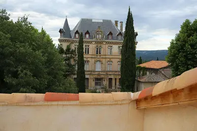 a large building behind a concrete wall with trees at GitesLuberon 5 in Charleval