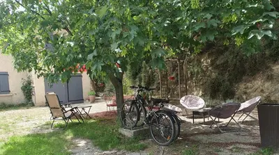 a bicycle parked next to two chairs under a tree at Les Marronniers Charmant petit appartement a La Tour d'Aigues Vaucluse in La Tour-dʼAigues