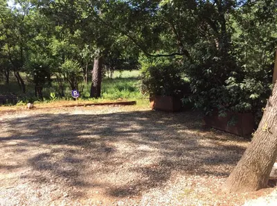 a shady park with a tree and a sign at Le Bois De La Cour in Roussillon