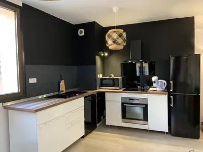 a kitchen with black walls and white cabinets and a refrigerator at La parenthèse sur la sorgue in LʼIsle-sur-la-Sorgue