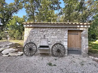 a small stone building with a wooden door and wheels at La villa dans les arbres - Triangle d'or du Luberon in Ménerbes