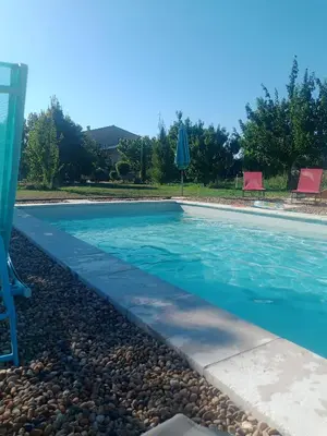 a swimming pool with blue water and rocks at Gite Le Petit Luberon LISIANTHUS in Cabrières-dʼAvignon
