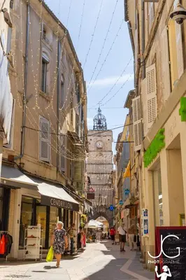 a woman walking down a city street with a clock tower at Le Romarin - Hypercentre Studio - Clim - WiFi in Apt
